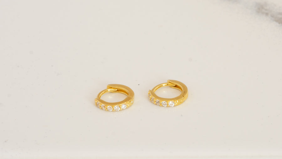 a pair of gold huggie hoop earrings made of cz stones