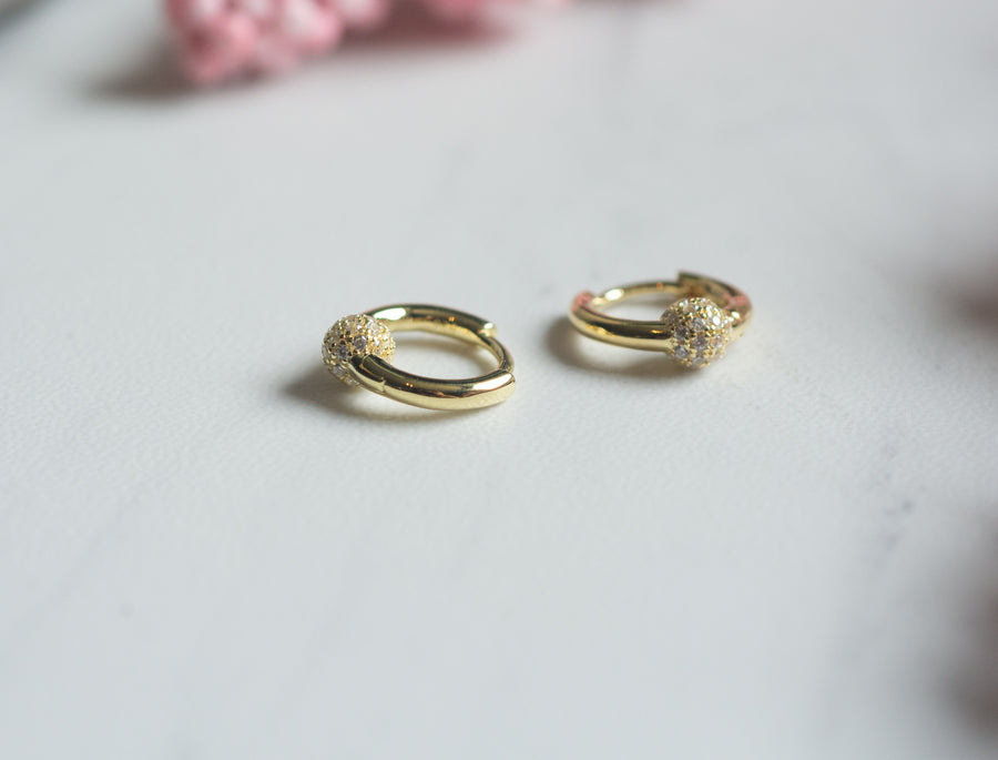 a pair of gold huggies with a cz ball charm 