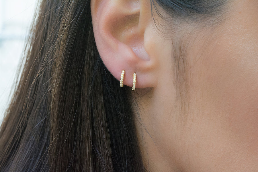 a model wearing two small huggie hoop earrings made of pave cubic zirconia stones 