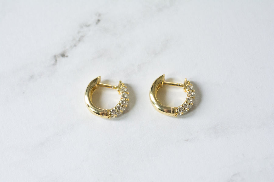 a pair of thick and small, gold, huggie style hoop earrings that have cubic zironia stones in front 