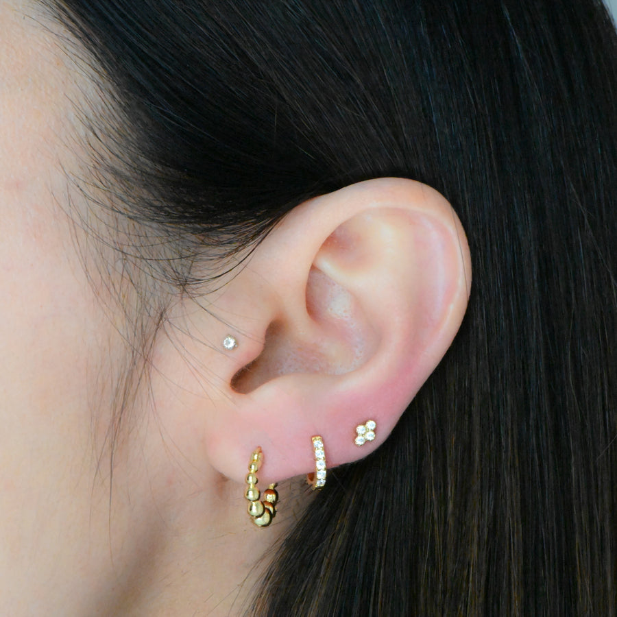 stacked huggie earrings featuring a model wearing a pair of small gold beaded huggie hoops, a diamond huggie and a four stone stud