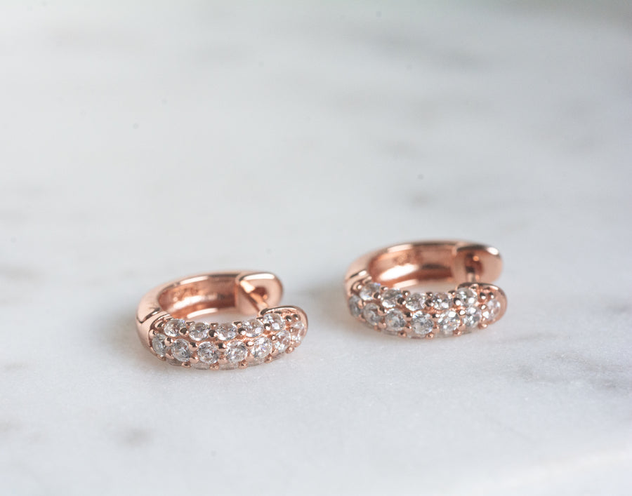 a pair of rose gold small huggie hearings with cubic zirconia stones 
