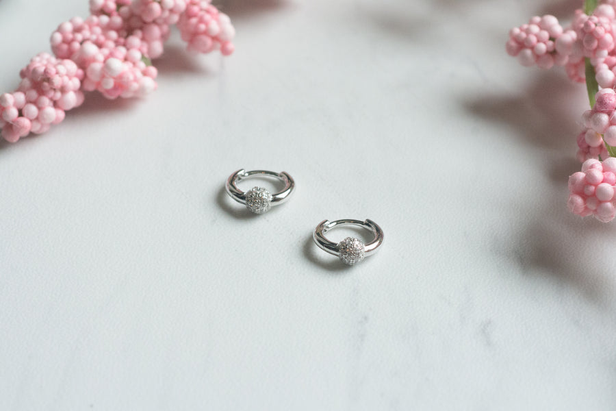 a pair of silver huggies with a pave ball charm design 